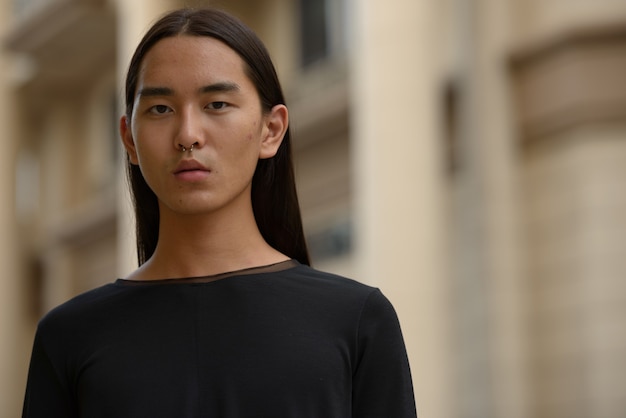 Gesicht des jungen asiatischen Mannes mit langen Haaren in der Stadt