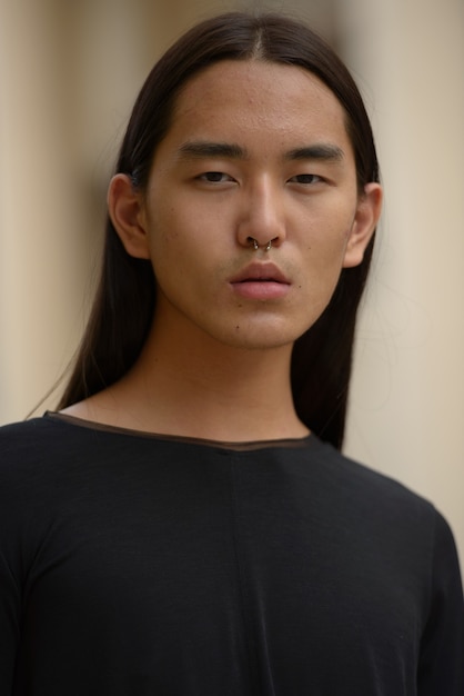 Gesicht des jungen asiatischen Mannes mit langen Haaren in der Stadt