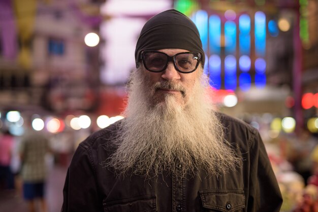 Gesicht des reifen bärtigen Touristenmannes, der nachts Sonnenbrille in Chinatown trägt