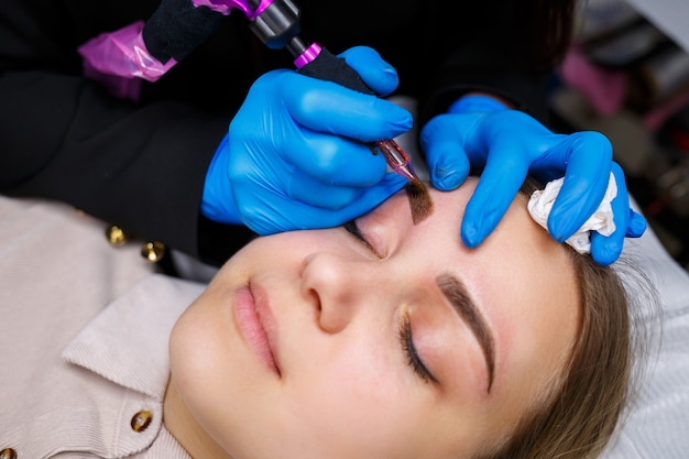 Gesicht einer schönen Frau mit buschigen Augenbrauen in einem Schönheitssalon. Permanent Make-up für die Augenbrauen. Kosmetikerin macht Augenbrauentattoo für Frauen. Schönheitsverfahren.