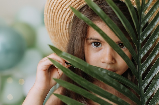 Gesicht eines kleinen Mädchens, umgeben von tropischen Blättern Nahaufnahmeporträt eines schönen dunkelhäutigen Babys