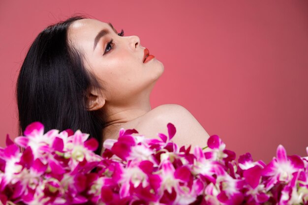 Gesicht erschossen Porträt der Mode 20er Jahre Asiatin schöne schwarze Haare drücken das sinnliche glückliche Lächeln aus. Mädchen halten purpurrote Orchideenblume für Hautpflegekosmetik und -behandlung über rosa Hintergrund