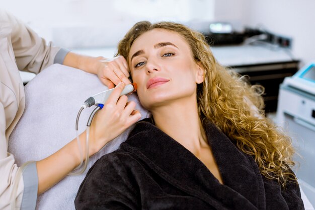 Gesicht Hautpflege. Nahaufnahme der hübschen blonden lockigen Frau, die Gesichts-Hydro-Mikrodermabrasions-Peeling-Behandlung an der Kosmetik-Spa-Klinik erhält.