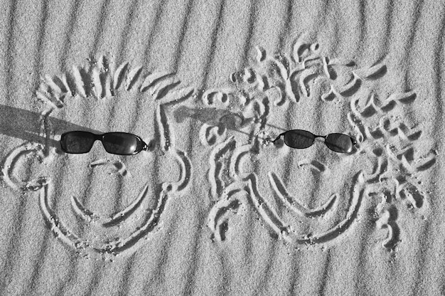 Gesicht im Sand am Strand mit Sonnenbrille gezeichnet Sand mit Wellenmuster