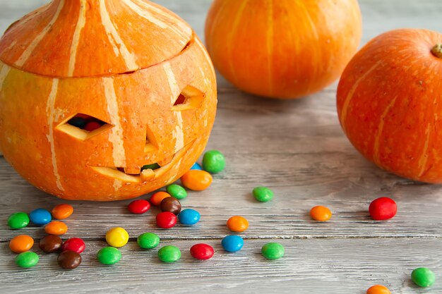 Gesicht in Kürbis mit Bonbonschokolade auf grauem hölzernem Hintergrund geschnitzt. Halloween