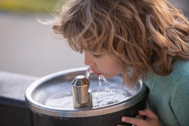 Gesicht Nahaufnahme Porträt des Kindes Trinkwasser aus dem Wasserhahn oder Wasser im Freien im Park Nahaufnahme Porträt des Kindes, das durstiges Kind trinkt