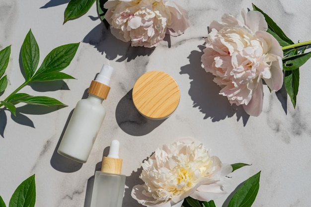 Gesichts- und Augenfeuchtigkeitscreme und -serum in einer Glasflasche und Glas- und Pfingstrosenblumen auf hellem Marmorhintergrund Konzept öko-biologische Naturkosmetikprodukte für die Hautpflege