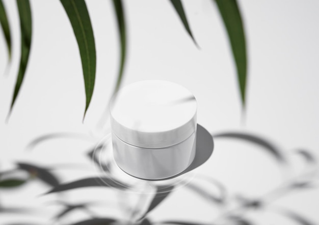 Gesichts- und Körpercreme in einem weißen Glas auf einem hellen Hintergrund mit Blättern und hartem Schatten
