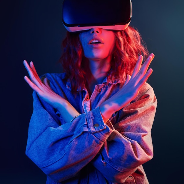 Gesichtsausdruck eines jungen Mädchens mit Virtual-Reality-Brille auf dem Kopf in rotem und blauem Neon im Studio
