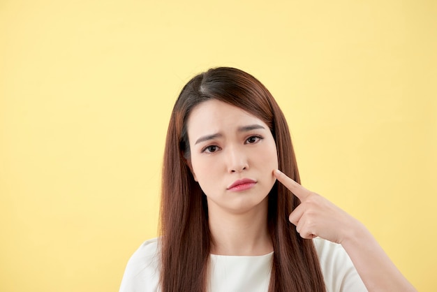 Gesichtshautproblem - junge Frau unglücklich berührt ihre Haut isoliert, Konzept für die Hautpflege, asiatisch