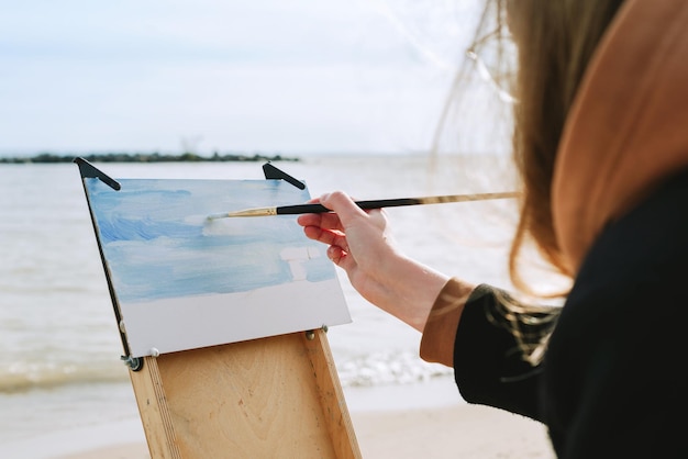 Gesichtslose Aufnahme einer weiblichen Zeichnung an einem Strand en Plein-Air-Künstler