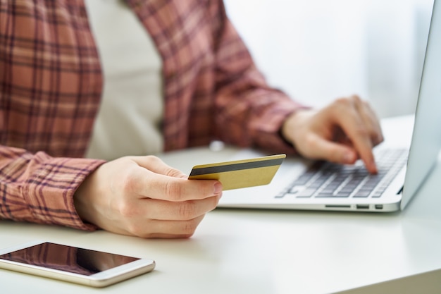 Gesichtslose Frau, die beim Einkaufen im Internet auf dem Laptop mit Debitkarte bezahlt