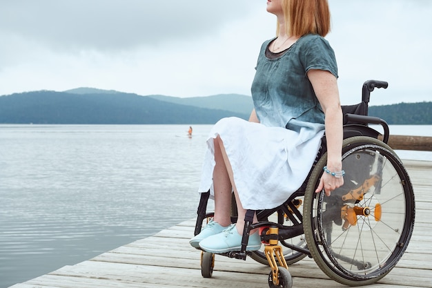 Gesichtslose Frau im Rollstuhl mit schönem Meer- oder Seeblick.