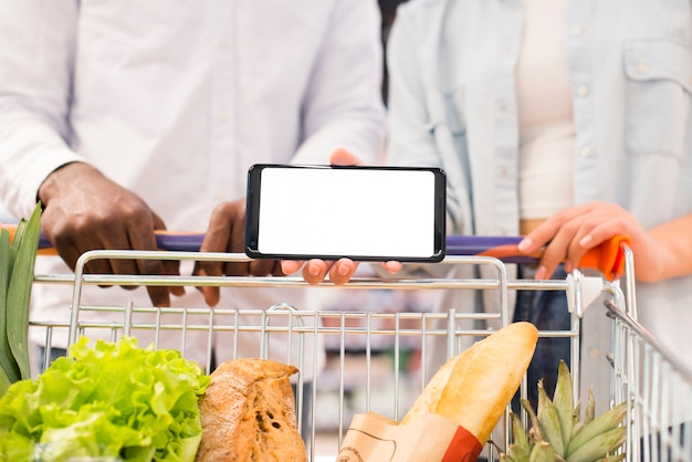 Gesichtslose Paare mit dem Warenkorb, der Smartphone am Supermarkt hält