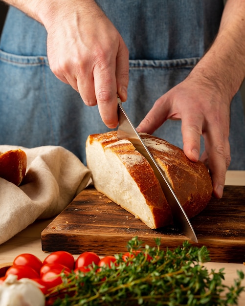 Gesichtsloser Mann, der frisches selbstgebackenes knuspriges Brot mit großem Messer schneidet