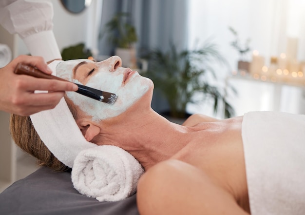 Gesichtsmaske Hand und Frau im Spa mit Hautpflege für organische Behandlungen Kosmetika oder Dermatologie im Bett Entspannen Sie sich reife Kunden und Masseurin mit Pinsel für Schönheit Wellness oder luxuriöse Gesichtspflege im Resort