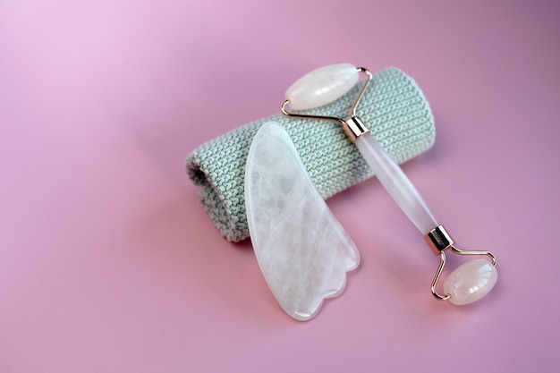 Gesichtsmassage-Set. Gesichtsroller und Gua-Sha-Massagegerät aus natürlichen rosa Steinen, Wohlbefinden, Gesichts-Fitness-Konzept, stilvolle monochrome Karte, Luxusbanner.