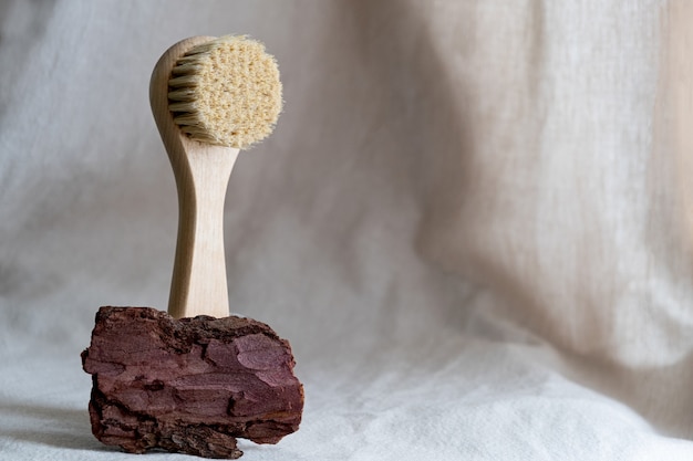 Gesichtsmassagebürste mit Naturborsten auf Leinenhintergrund mit Rinde und getrockneten Blumen. umweltfreundliches Kosmetikkonzept.