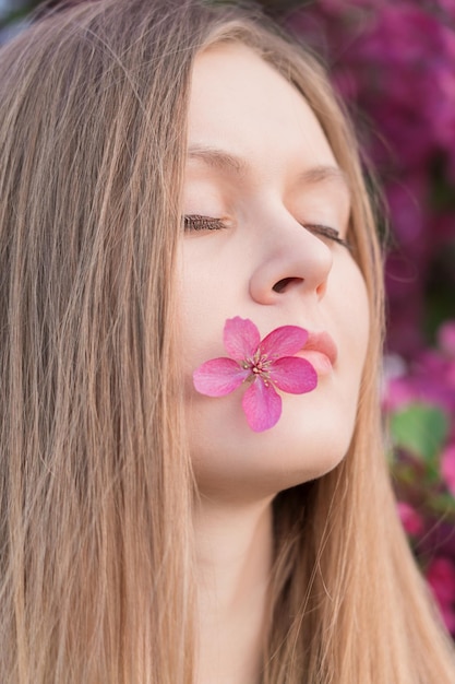 Gesichtsporträt einer jungen blonden Frau mit geschlossenen Augen und einem meditativen Lächeln mit rosa Blume