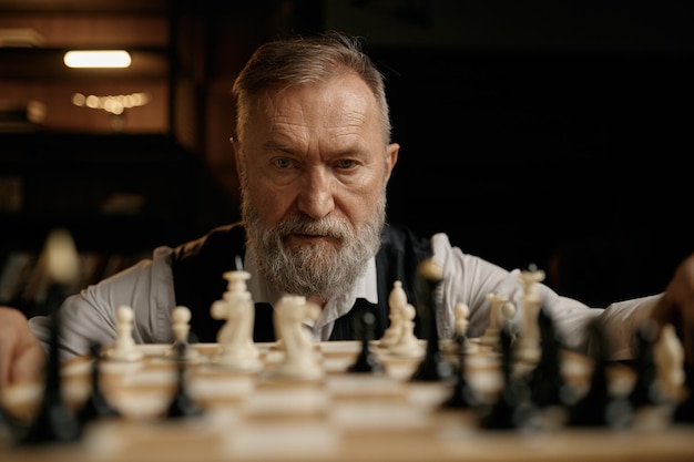 Gesichtsporträt eines selbstbewussten älteren Mannes, der während eines Freundschaftsspiels Schachfiguren an Bord betrachtet