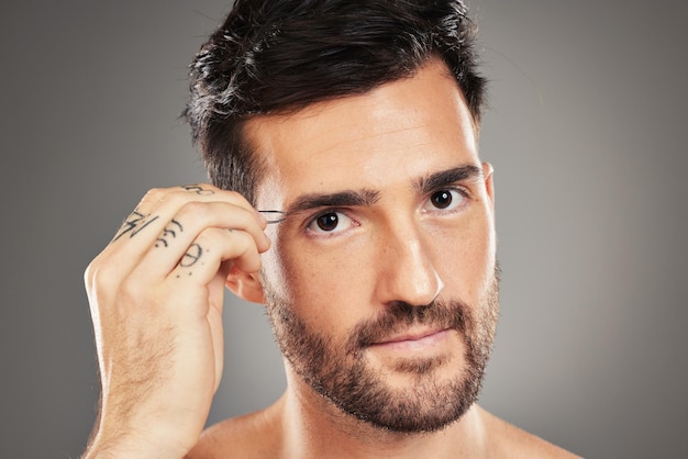 Gesichtsporträt und Pinzette mit einem Mannmodell, das seine Augenbrauen im Studio auf grauem Hintergrund zupft Hautpflege-Wellness und Luxus mit einem hübschen jungen Mann, der seine Augenbrauenhaare zur Pflege zupft