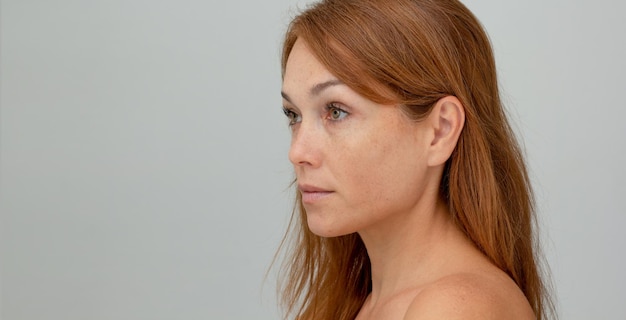 Gesichtsprofil einer Frau mittleren Alters mit rötlichem Haar auf grauem Hintergrund