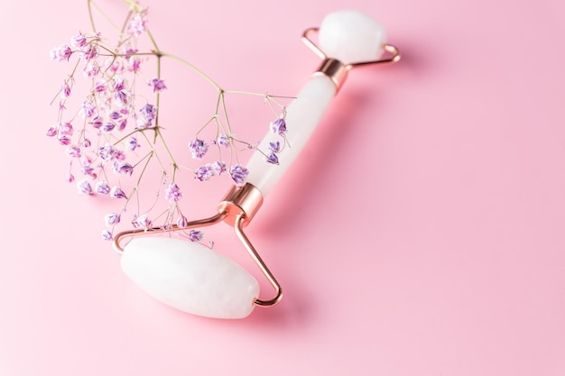 Foto gesichtsroller und gypsophila-blumen auf rosa hintergrund massage-werkzeug für gesichtshautpflege spa-schönheit