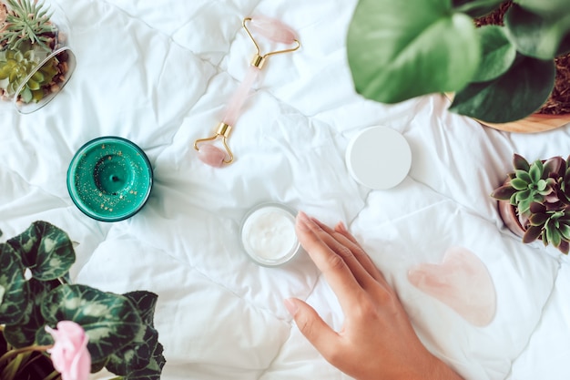 Gesichtsschönheitsrolle, Creme, Serum und Grünpflanzen auf weißem Bett. Beauty-Routine-Konzept am Morgen