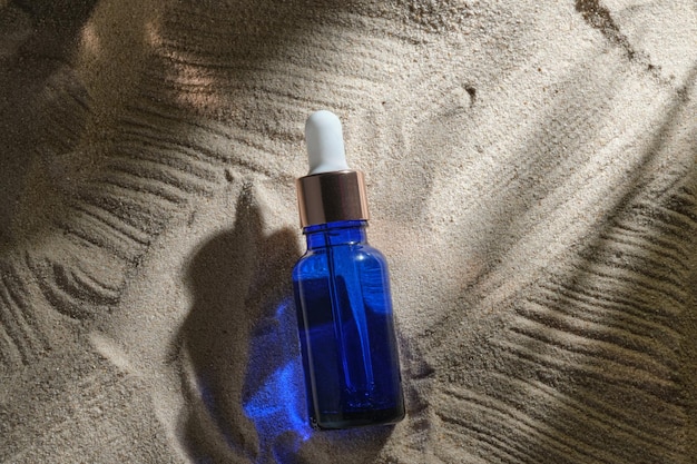 Gesichtsserum aus Glasflasche mit einer Pipette auf natürlichem Hintergrund mit Sand Ätherisches Öl zur feuchtigkeitsspendenden Körperhaut-Attrappe von Schönheitsmode-Kosmetikflaschen-Tropfprodukten mit Hautpflegekonzept
