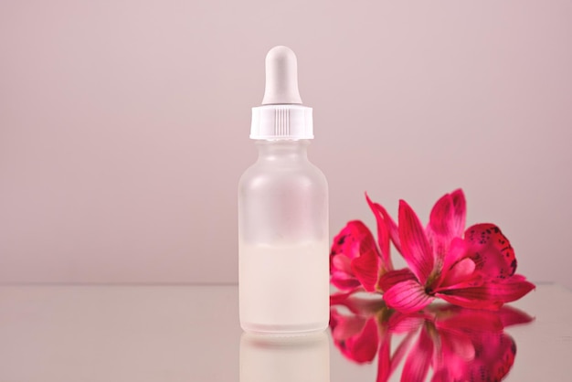 Gesichtsserumöltropfen mit Tropfglasflasche Pipette rosa Blumen Hintergrund Nahaufnahme