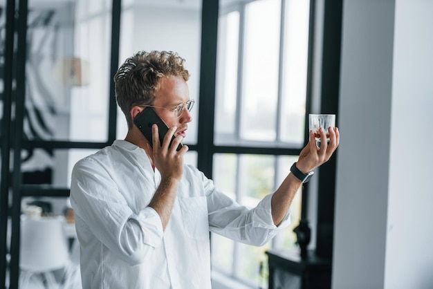 Gespräche per Telefon Kaukasischer junger Mann im eleganten weißen Hemd zuhause zu Hause