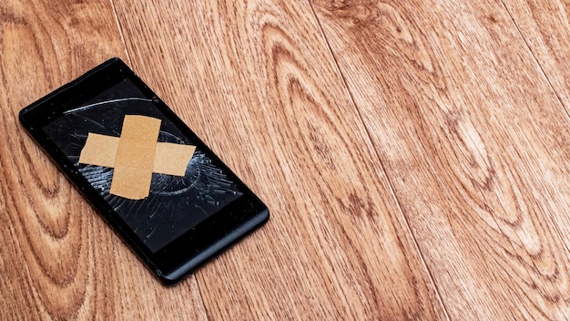 Gesso adesivo em uma tela de telefone quebrada na mesa de madeira