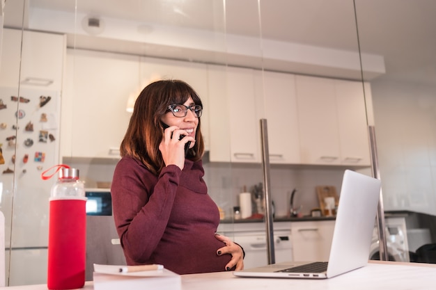 Foto gestante jovem em teletrabalho de casa com o computador devido às dificuldades de trabalho, com atitude positiva no atendimento ao trabalho