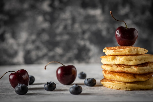 Gestapelte Pfannkuchen mit Kirschen und Blaubeeren auf einem grauen Vintage-Holztisch Platz für Text