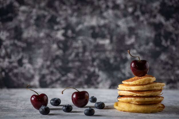 Gestapelte Pfannkuchen mit Kirschen und Blaubeeren auf einem grauen Vintage-Holztisch Platz für Text