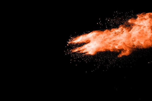 Gestartete orange Farbenpulverexplosion auf schwarzem Hintergrund.