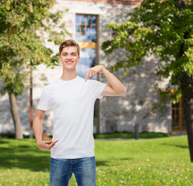 Geste, Werbung, Sommerferien, Bildung und Personenkonzept - lächelnder junger Mann in leerem weißem T-Shirt, der mit dem Finger auf sich selbst über dem Campushintergrund zeigt