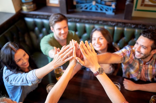 Foto gesten-, menschen- und freundschaftskonzept - glückliche freunde, die bier trinken und in der bar oder im pub high five machen