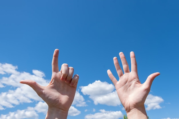 Gestennahaufnahme der Hand einer Frau, die eine offene Handfläche und zwei Finger einzeln auf blauem Himmelshintergrund mit Wolken zeigt, Nummer sieben ist das Symbol der Gebärdensprache