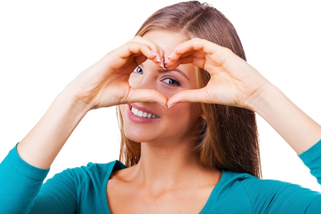 Gesticular el corazón del dedo. Hermosa mujer joven mirando a la cámara y gesticulando el corazón del dedo mientras está de pie aislado en blanco