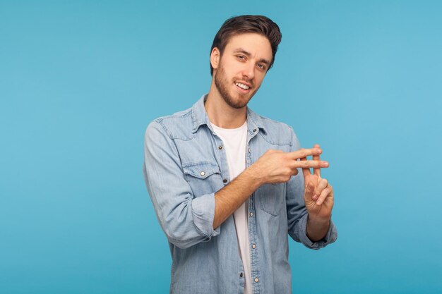 Gesto de hashtag. Retrato de um homem bonito alegre na camisa jeans do trabalhador cruzando os dedos, mostrando o símbolo de hash, marcando a famosa mensagem da internet, blog viral. tiro de estúdio isolado em fundo azul