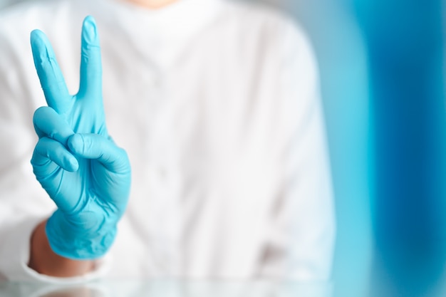 Foto gesto de mão de médico com luvas azuis, sinal para lutar