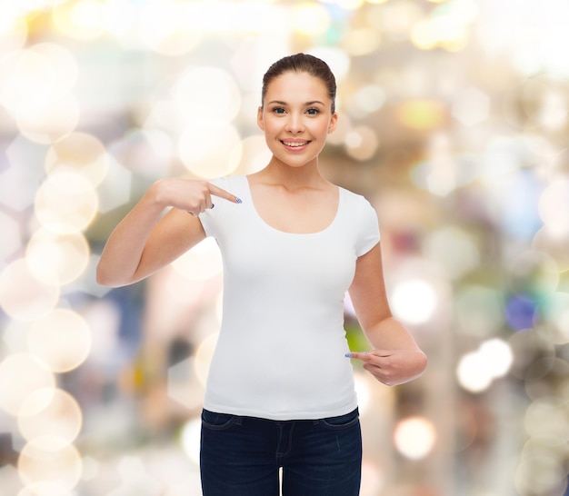 gesto, feriados, publicidade e conceito - jovem sorridente em camiseta branca em branco apontando dedos sobre si mesma sobre fundo cintilante