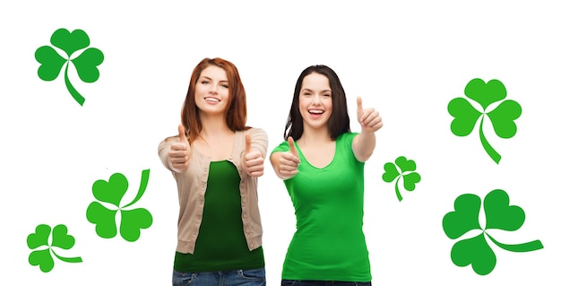 Gesto, feriados, st. dia de patricks e conceito de pessoas felizes - duas meninas sorridentes mostrando os polegares sobre fundo branco com trevo verde ou trevo