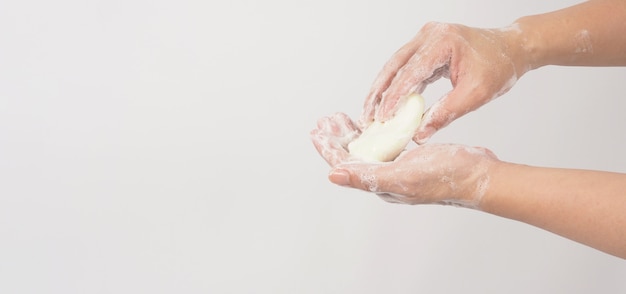Gesto de lavado de manos con jabón en barra y burbujas de espuma sobre fondo blanco.