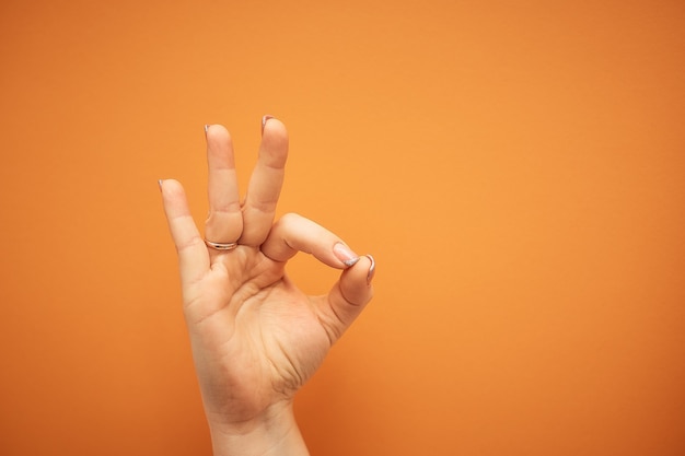 Foto gesto, mano femenina muestra signo ok aislado en naranja.