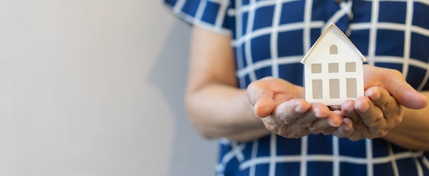 gesto de la mano de mujer senior para sostener el modelo de casa blanca para la inversión de vida y seguros