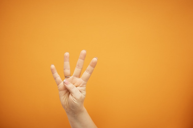 Gesto, mão feminina mostra quatro dedos isolados em laranja.