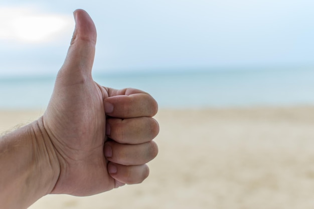 Foto gesto ok en el fondo de la playa levantó la parte superior del pulgar de una mano masculina