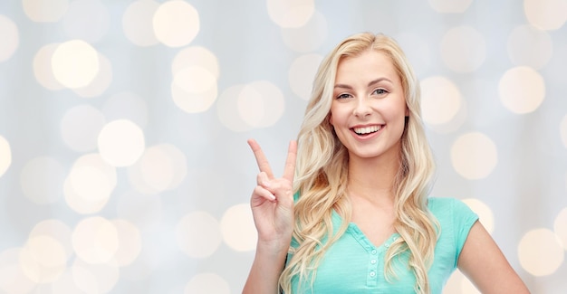 Gesto positivo y concepto de la gente: joven sonriente o adolescente que muestra el signo de la mano de la paz durante las vacaciones luces de fondo